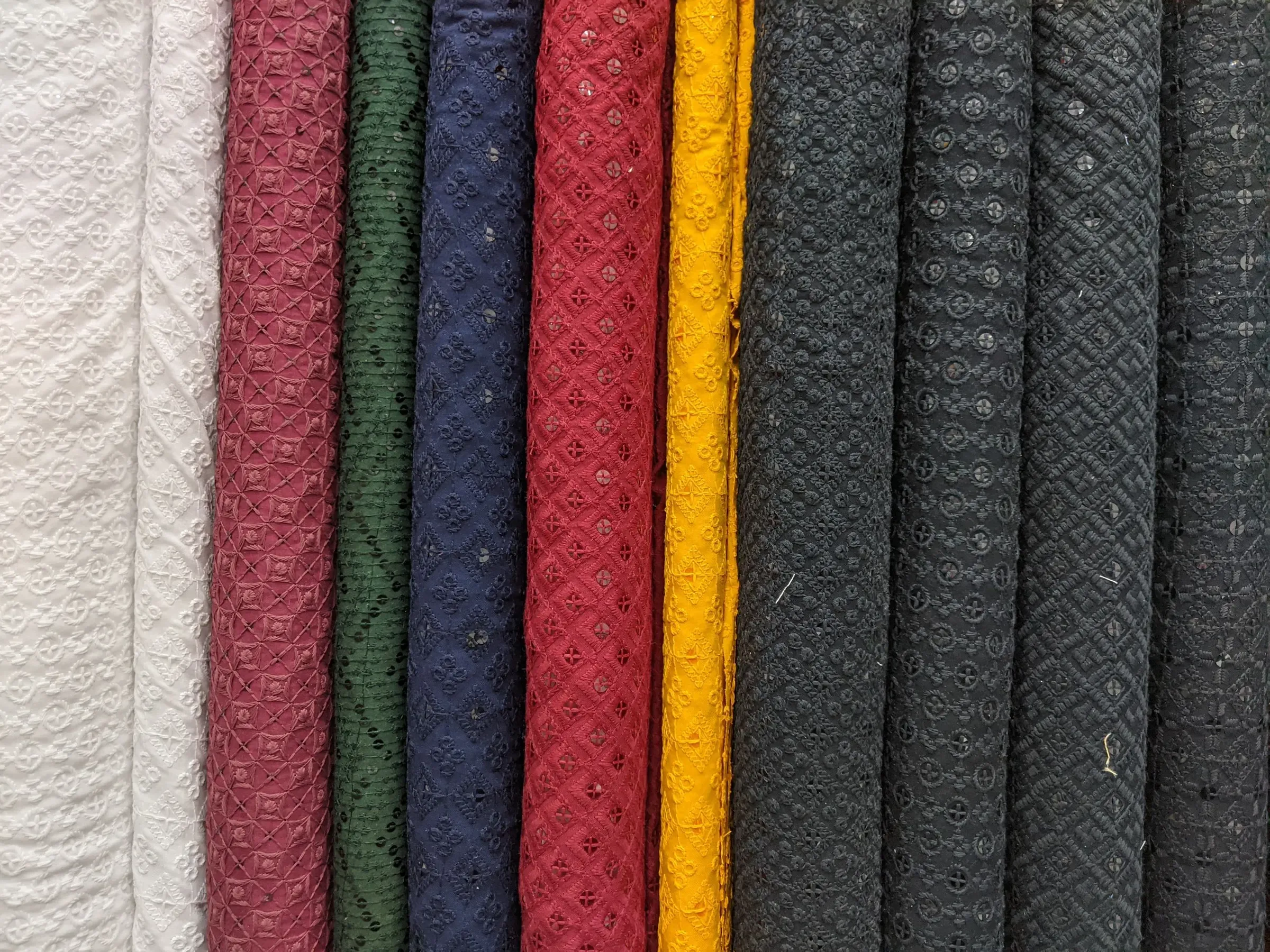 Rolls of chikan embroidered cotton in ivory, rose, bottle green, navy, red, haldi and black